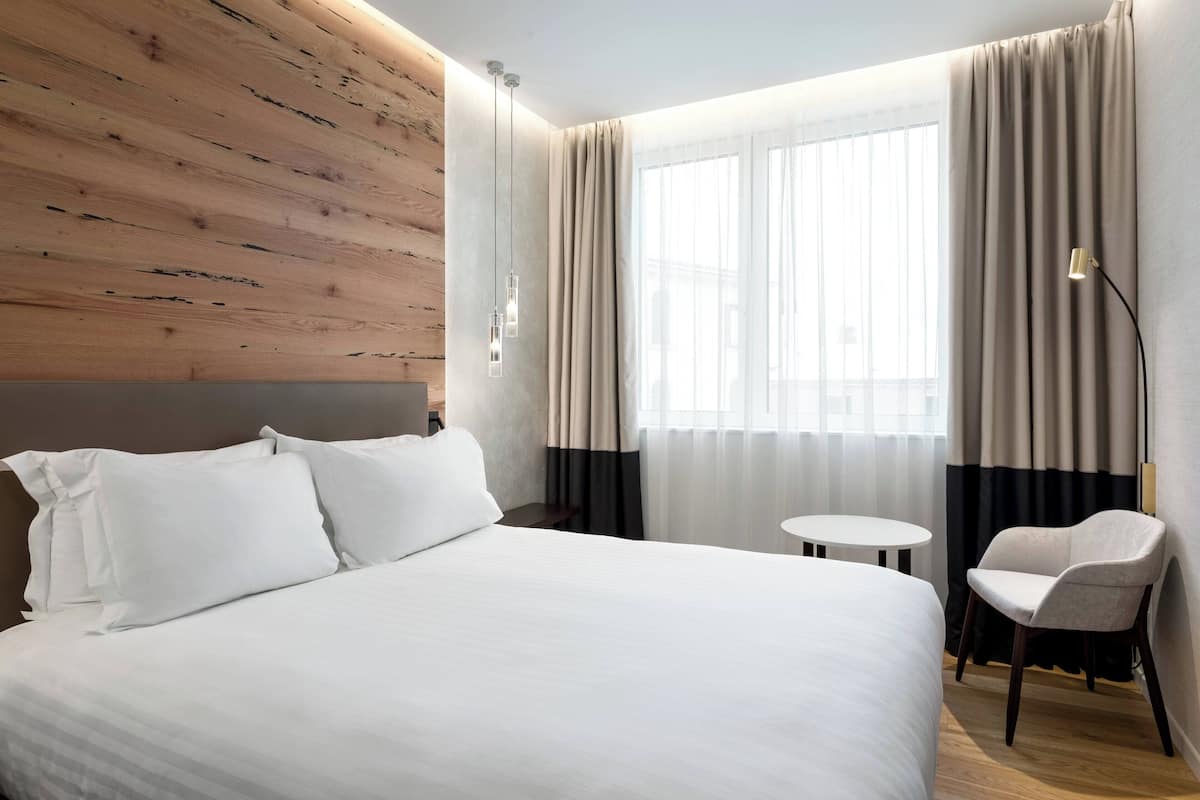 A hotel room with a large bed, a small round table, and a chair.