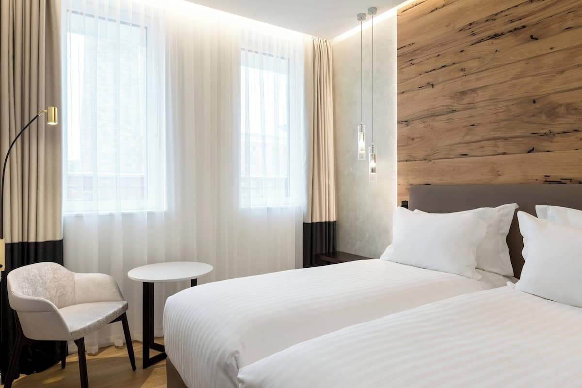 A hotel room with two beds, a small table, a chair, and a wooden accent wall.