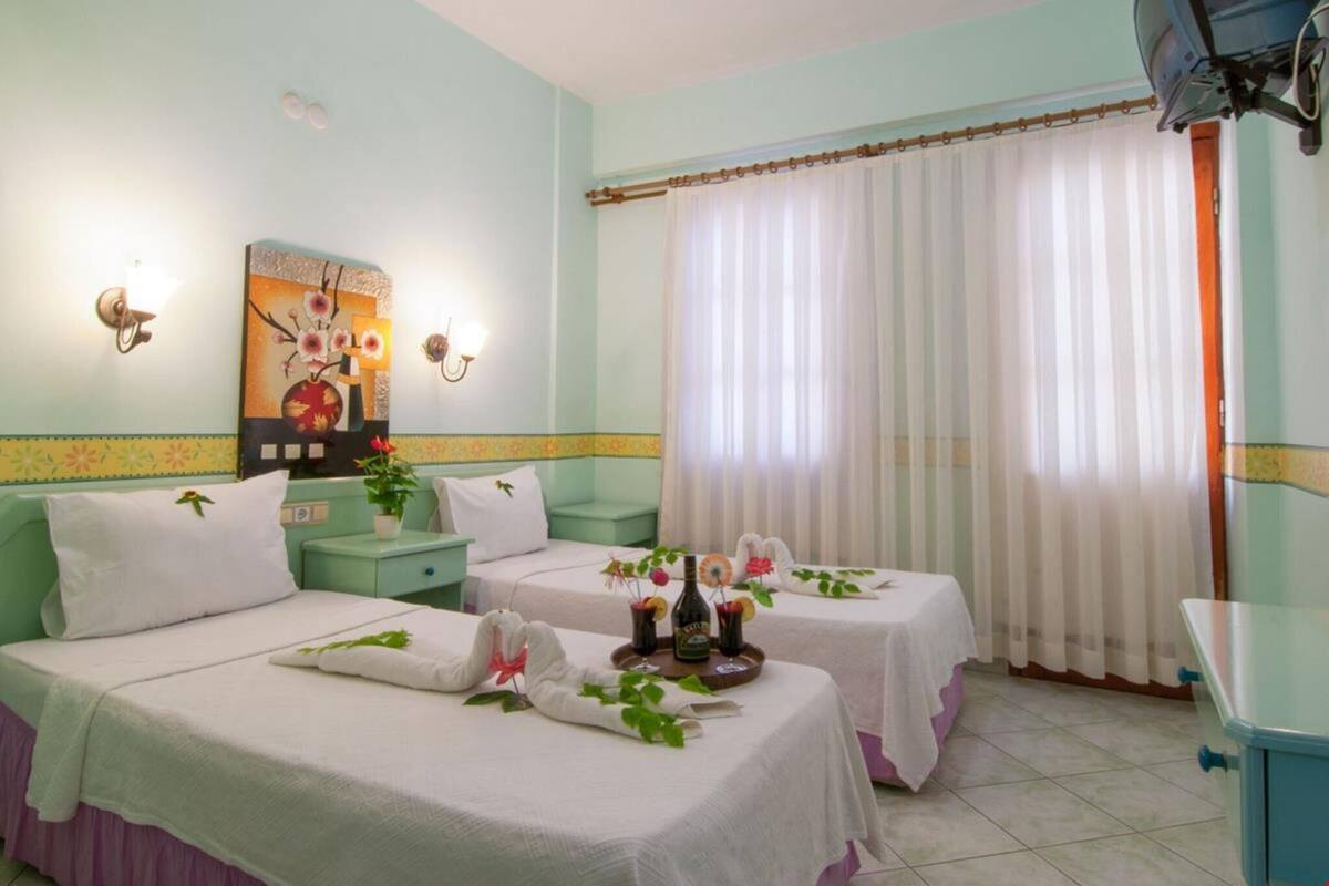 Ein Hotelzimmer mit zwei Betten, einem Bild an der Wand, einem Fenster mit Vorhängen und einer Minibar.