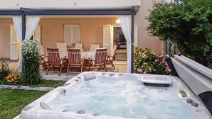 Een hottub in een overdekte buitenruimte met een tafel en stoelen, omgeven door groen en bloemen.