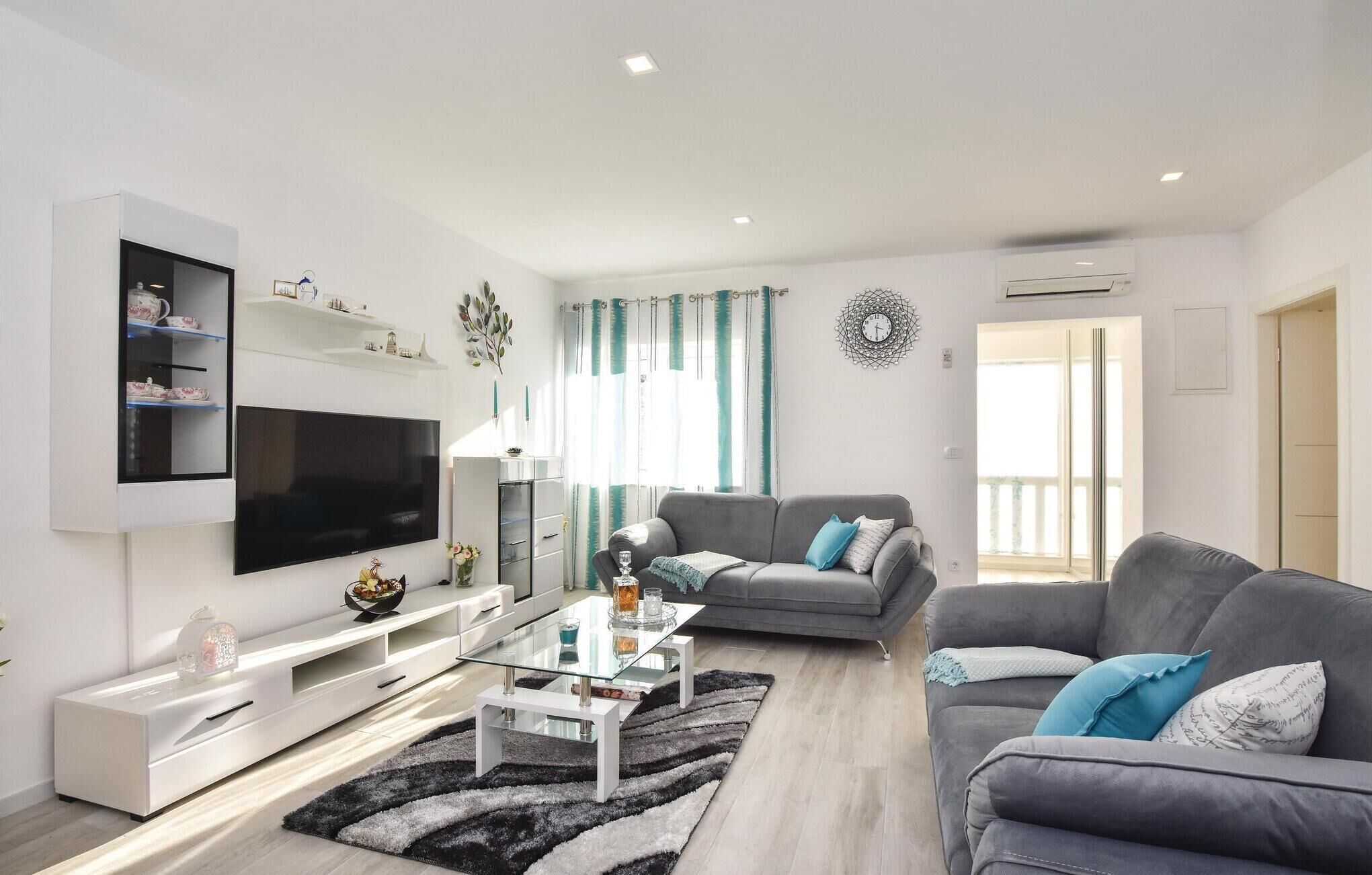 Una sala de estar moderna con un televisor de pantalla plana, sofás grises, una mesa de centro de vidrio y un mueble bajo en blanco.