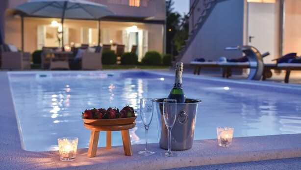 Een zwembadterras met een champagnefles, glazen, aardbeien en kaarsen.