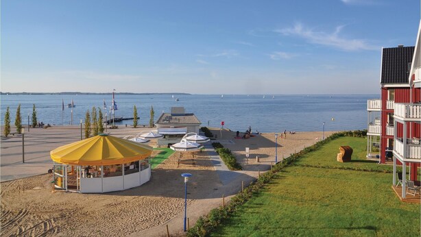 Une vue sur la plage avec une tente jaune, des tables de pique-nique et une zone herbeuse.