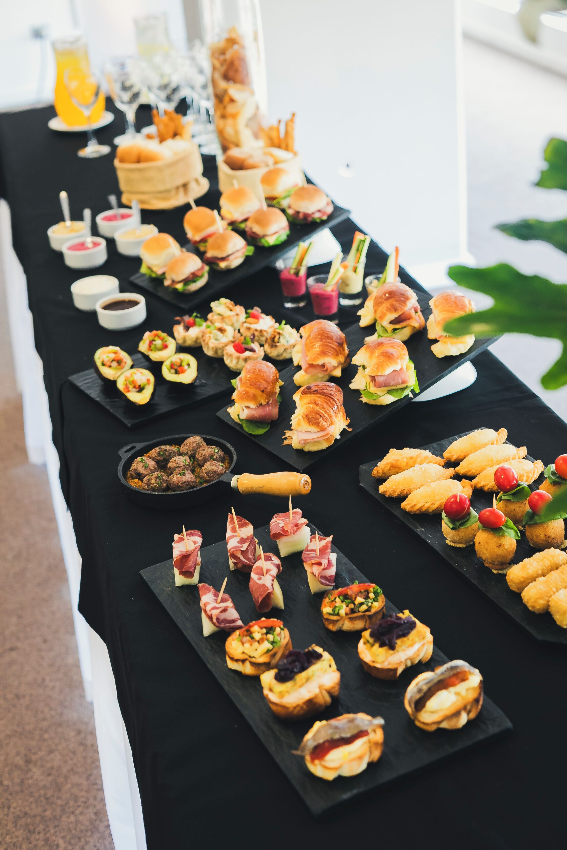 Uma mesa de buffet com diversos itens de comida, incluindo sanduíches, croissants e aperitivos.