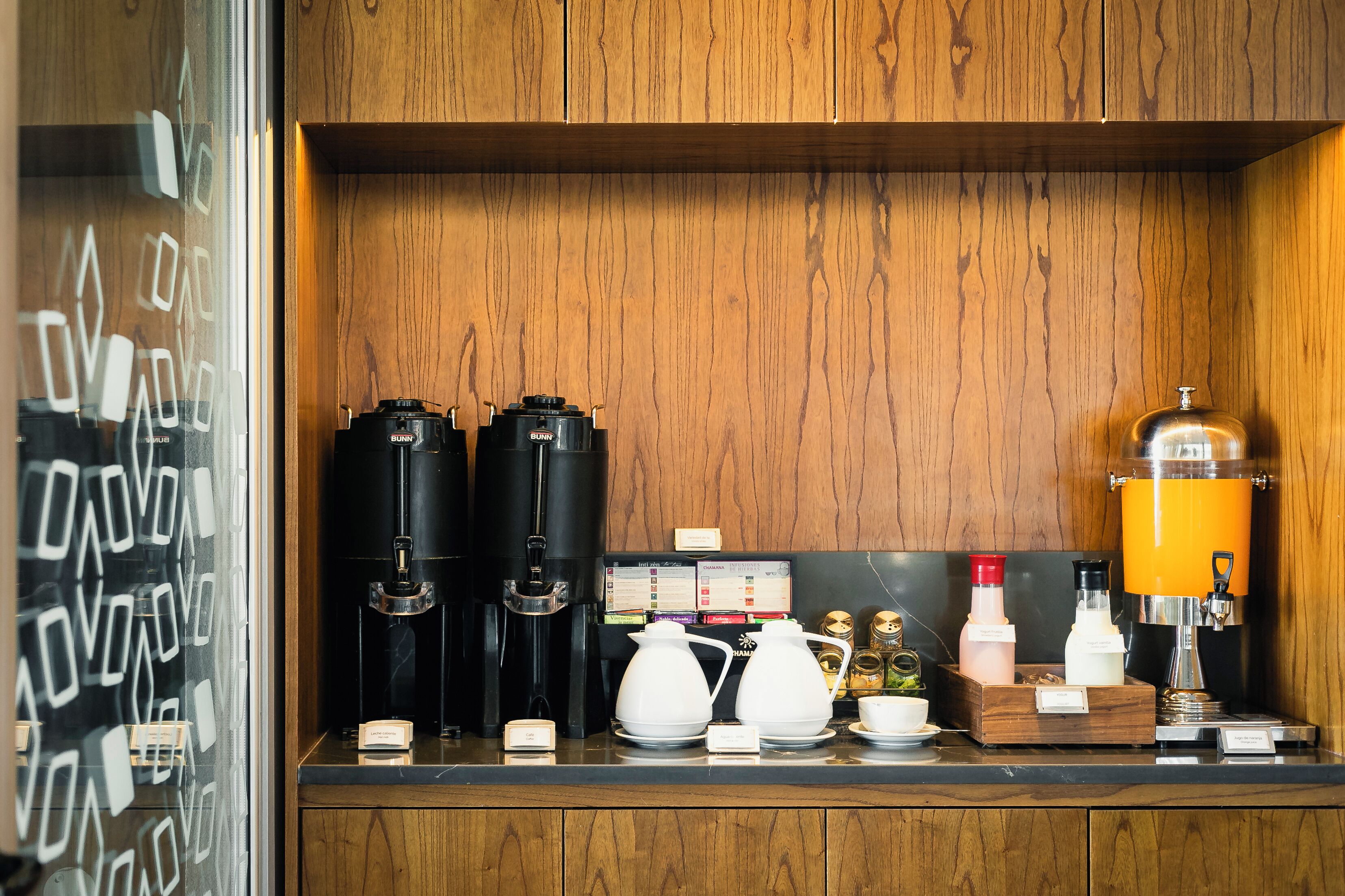 Una estación de café con varias cafeteras, una jarra de café y un espumador de leche.