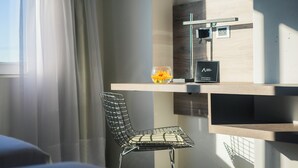 Una habitación moderna con un separador de vidrio, una silla de metal, una mesita con un jarrón de flores y un televisor de pared.