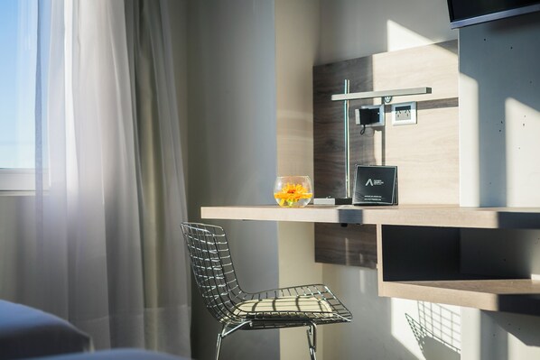 Una habitación moderna con un separador de vidrio, una silla de metal, una mesita con un jarrón de flores y un televisor de pared.