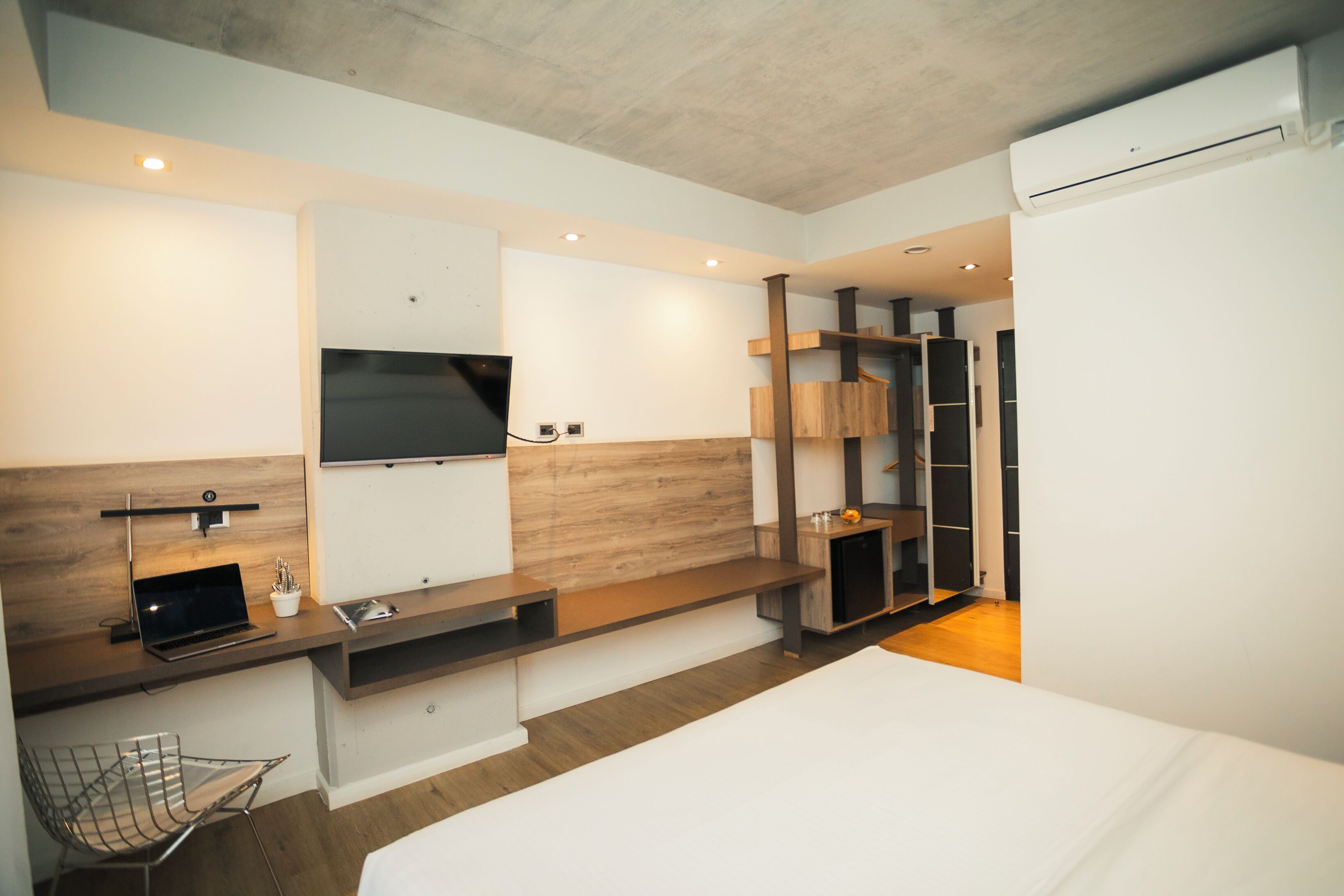 Una habitación de hotel moderna con una cama, un escritorio con una computadora portátil, un televisor montado en la pared y un armario.