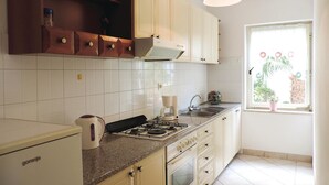 A kitchen with white cabinets, a gas stove, a kettle, and a window with a view of greenery. - Nice apartment in Rabac with house sea view (Rabac)