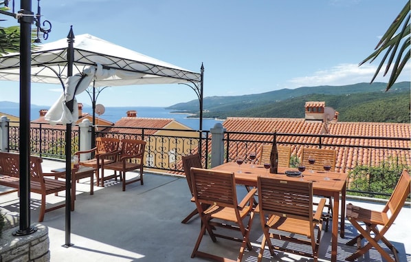 A terrace with wooden furniture, a white umbrella, and a view of the sea and hills. - Nice apartment in Rabac with house sea view (Rabac)