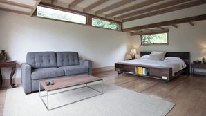 Un dormitorio con una cama, un sofá gris, una mesa de centro de madera y una mesita de noche con lámpara.