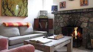 Una sala de estar acogedora con chimenea, un tablero de ajedrez, un sofá y una estantería.