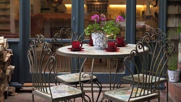 Una mesa redonda con cuatro sillas, una planta en maceta con flores y tazas rojas sobre la mesa.