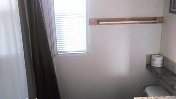 A small bathroom with a toilet, a shower curtain, a window, and a towel rack.