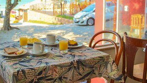 A table set with breakfast items, a glass of orange juice, and a view of the sea and mountains in the background. - Pousada Estrelas no Mar (Florianópolis)