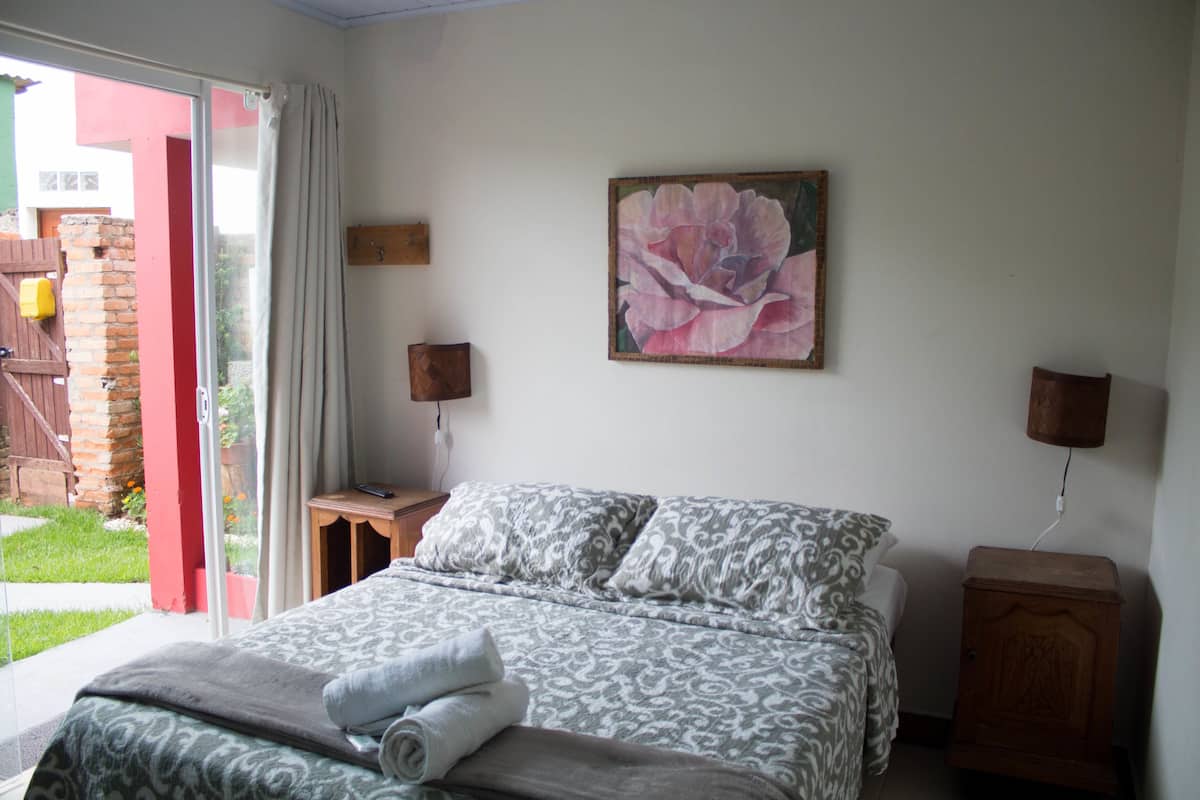 Un dormitorio con cama, mesita de noche, lámpara y un cuadro en la pared.