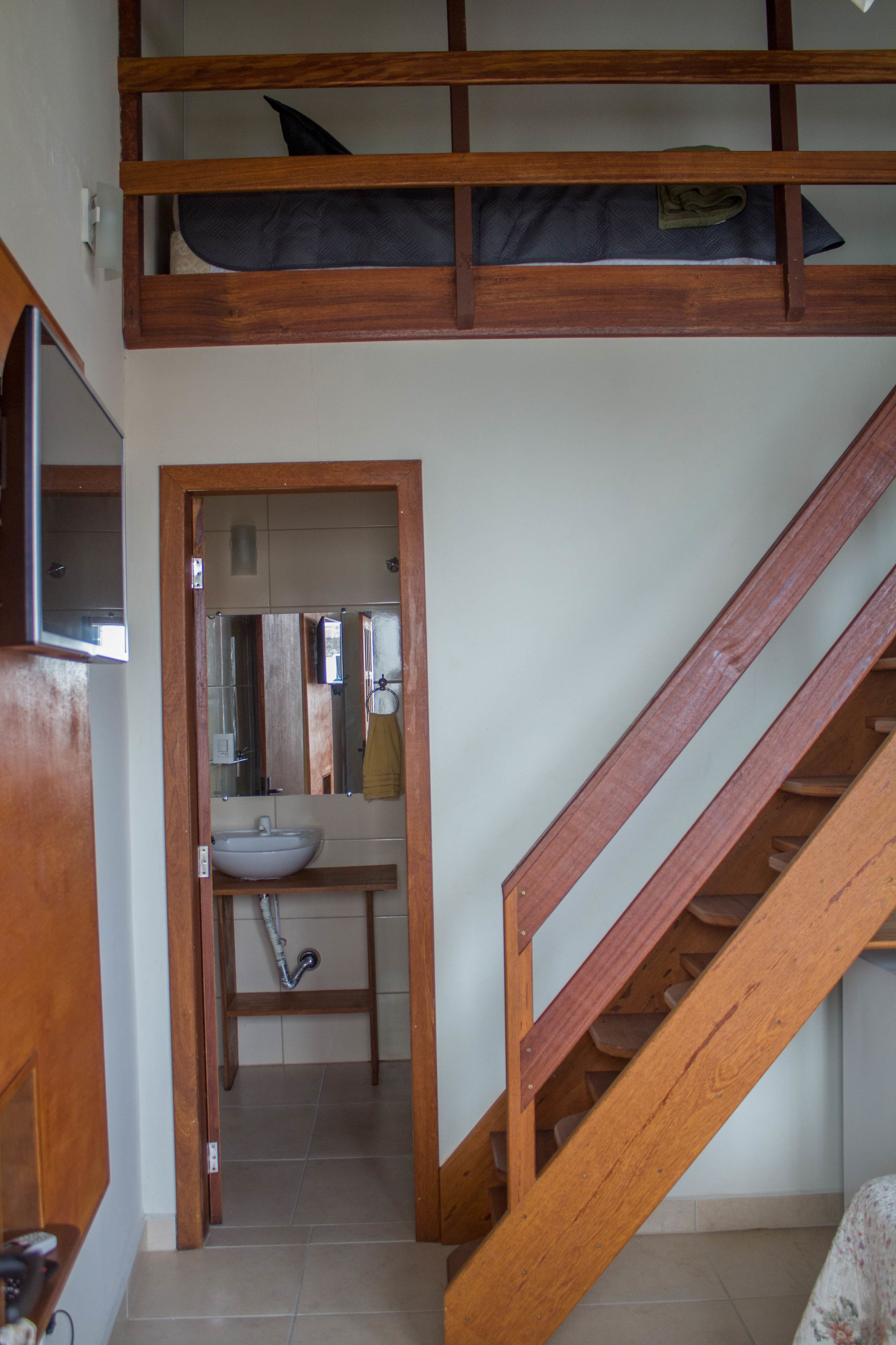 A room with a bunk bed, a bathroom with a sink and mirror, and a wooden staircase.