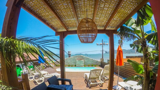 A covered outdoor seating area with a pool, wooden deck, and tropical plants. - Pousada Estrelas no Mar (Florianópolis)