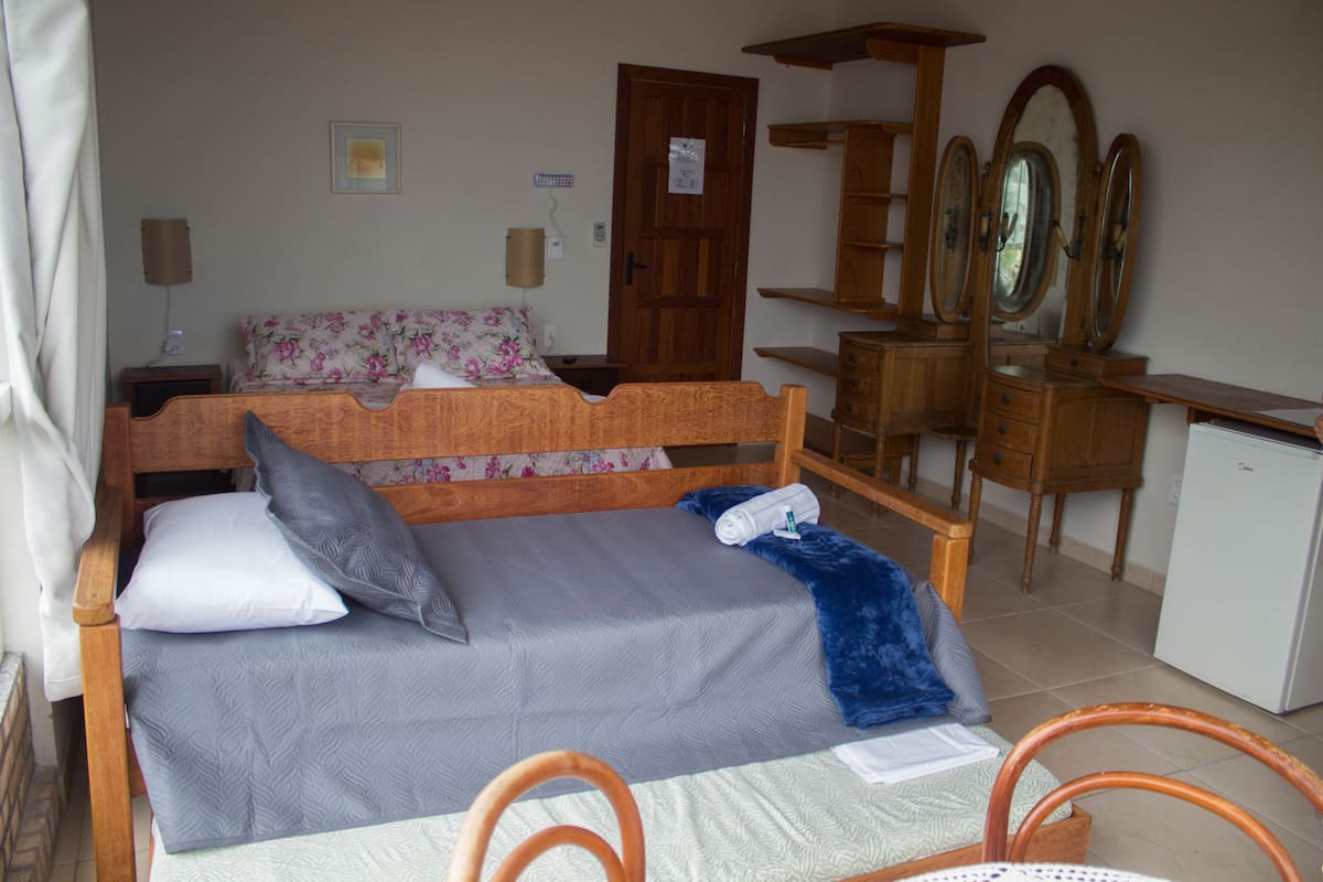 Un dormitorio con cama, cómoda, espejo y refrigerador pequeño.