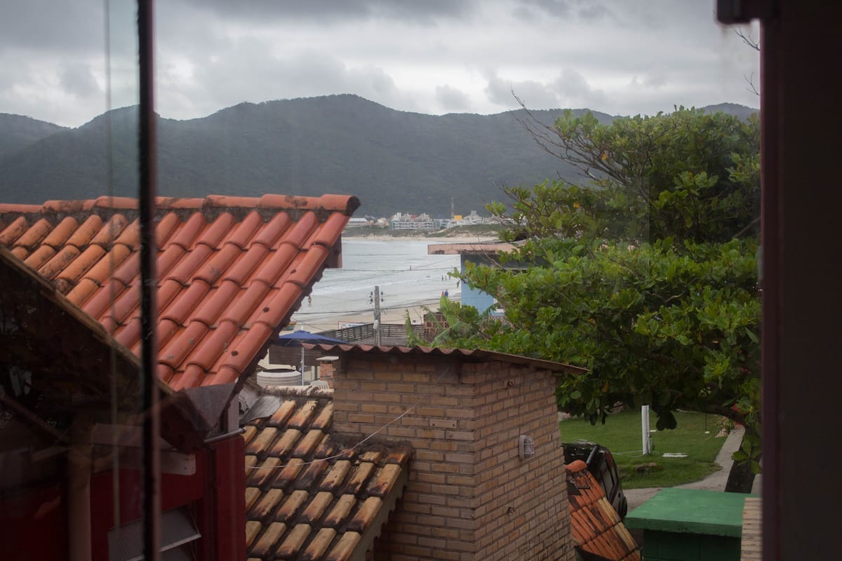 Vista de una zona costera con un edificio de ladrillo y techo de tejas, con vista a una masa de agua y montañas a lo lejos.