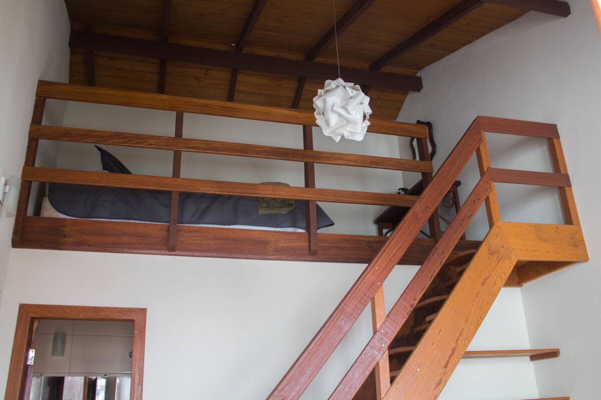 Una cama nido de madera con colchón y una lámpara colgante decorativa blanca.
