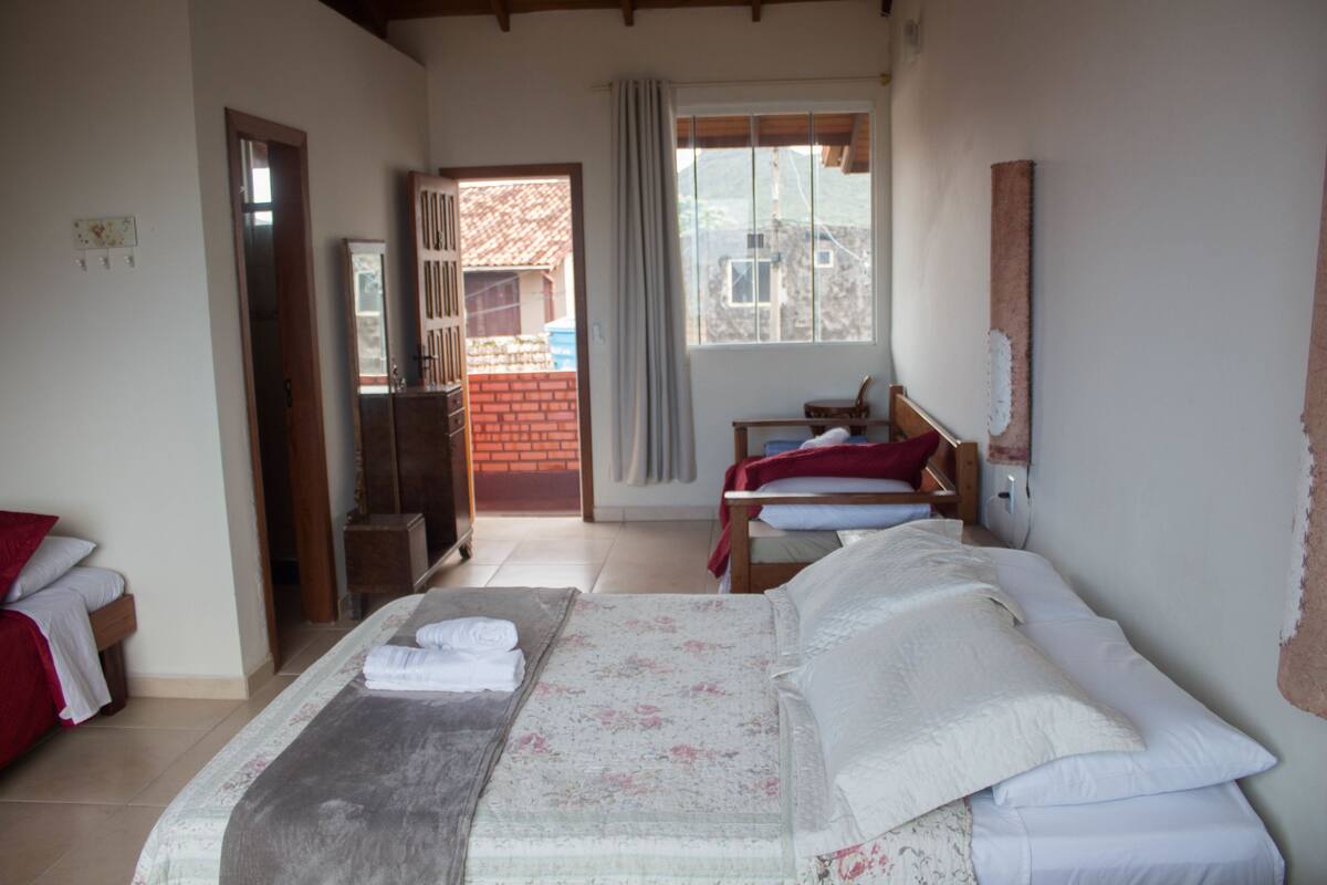 Un dormitorio con una cama grande, una mesita de noche de madera, una silla y una ventana con vistas a un edificio de ladrillo.
