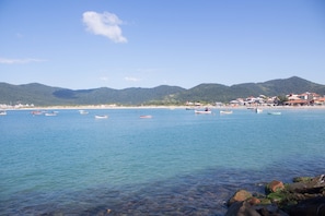 Un paisaje costero con barcos en aguas tranquilas, una playa arenosa y montañas al fondo.