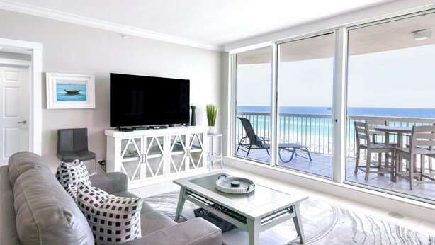 A modern living room with a large TV, a sofa, and a balcony with a view of the ocean. - Seaside charm in beachfront condo w/private balcony & beach service in Destin! (Destin)