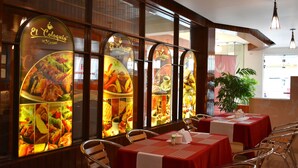 Restaurante con manteles rojos y sillas metálicas, mostrando un gran menú con imágenes de comida.