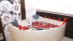 Una bañera grande independiente llena de agua y pétalos de rosa, rodeada de velas.