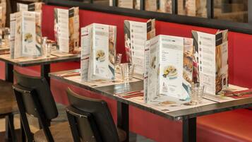 Interior de restaurante con asientos de tapicería roja, soportes para menú y sillas negras.