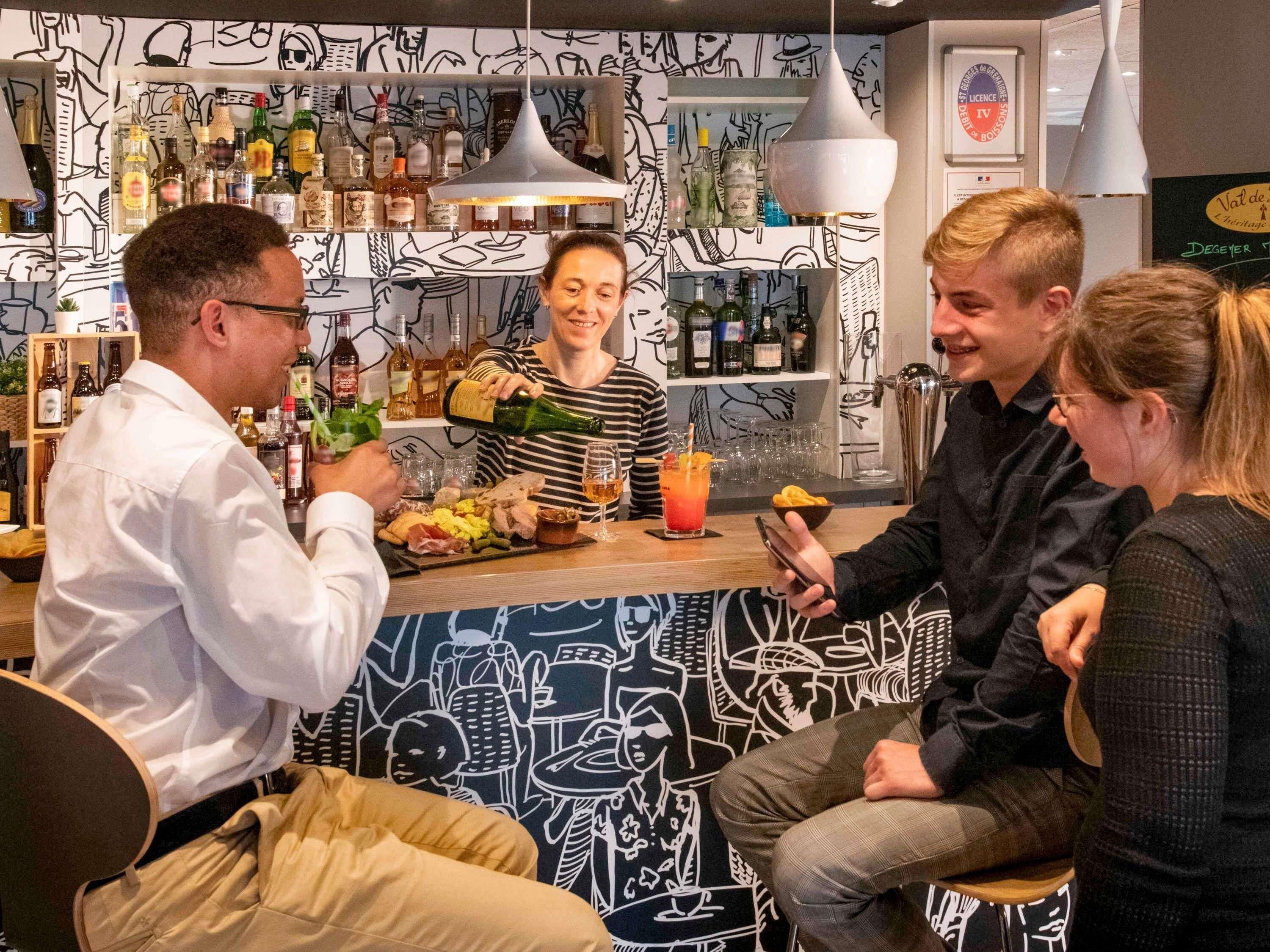 Zona de bar con diversas botellas, una persona sirviendo una bebida, y un mostrador con comida y un vaso.