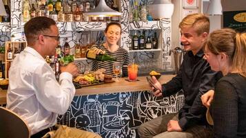 A bar area with a variety of bottles, a person pouring a drink, and a counter with food and a glass.