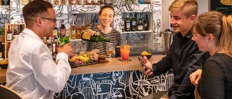Zona de bar con diversas botellas, una persona sirviendo una bebida, y un mostrador con comida y un vaso.