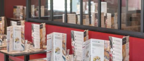 Ein Restaurantinnenraum mit gedeckten Tischen, Speisekarten und schwarzen Stühlen.