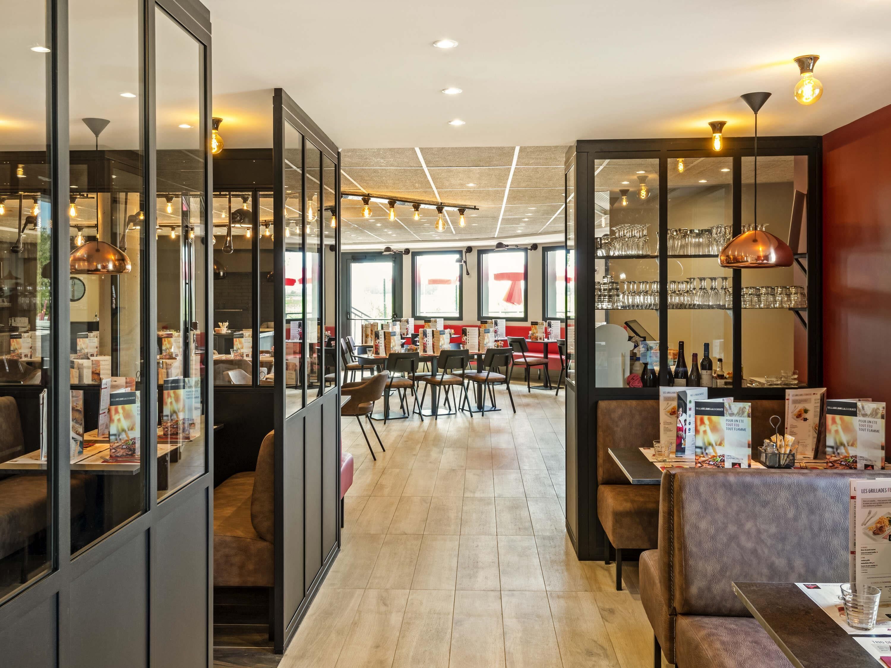 A modern restaurant interior with glass partitions, wooden flooring, and a variety of seating options including booths and tables.