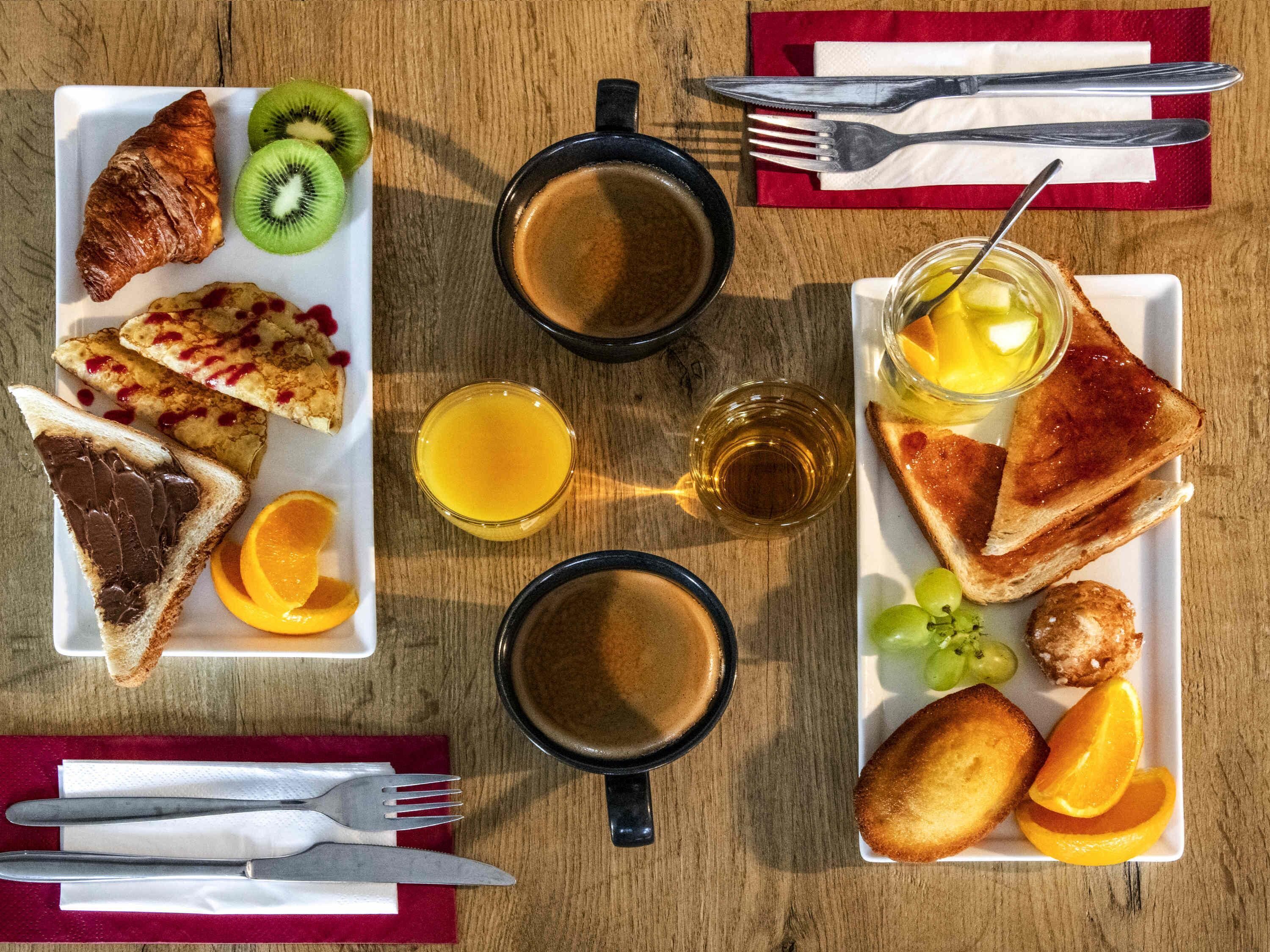 Une table en bois dressée pour le petit-déjeuner, avec des croissants, des toasts, des fruits et du café.