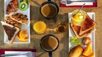 A breakfast setting with croissants, toast, fruit, and coffee on a wooden table.