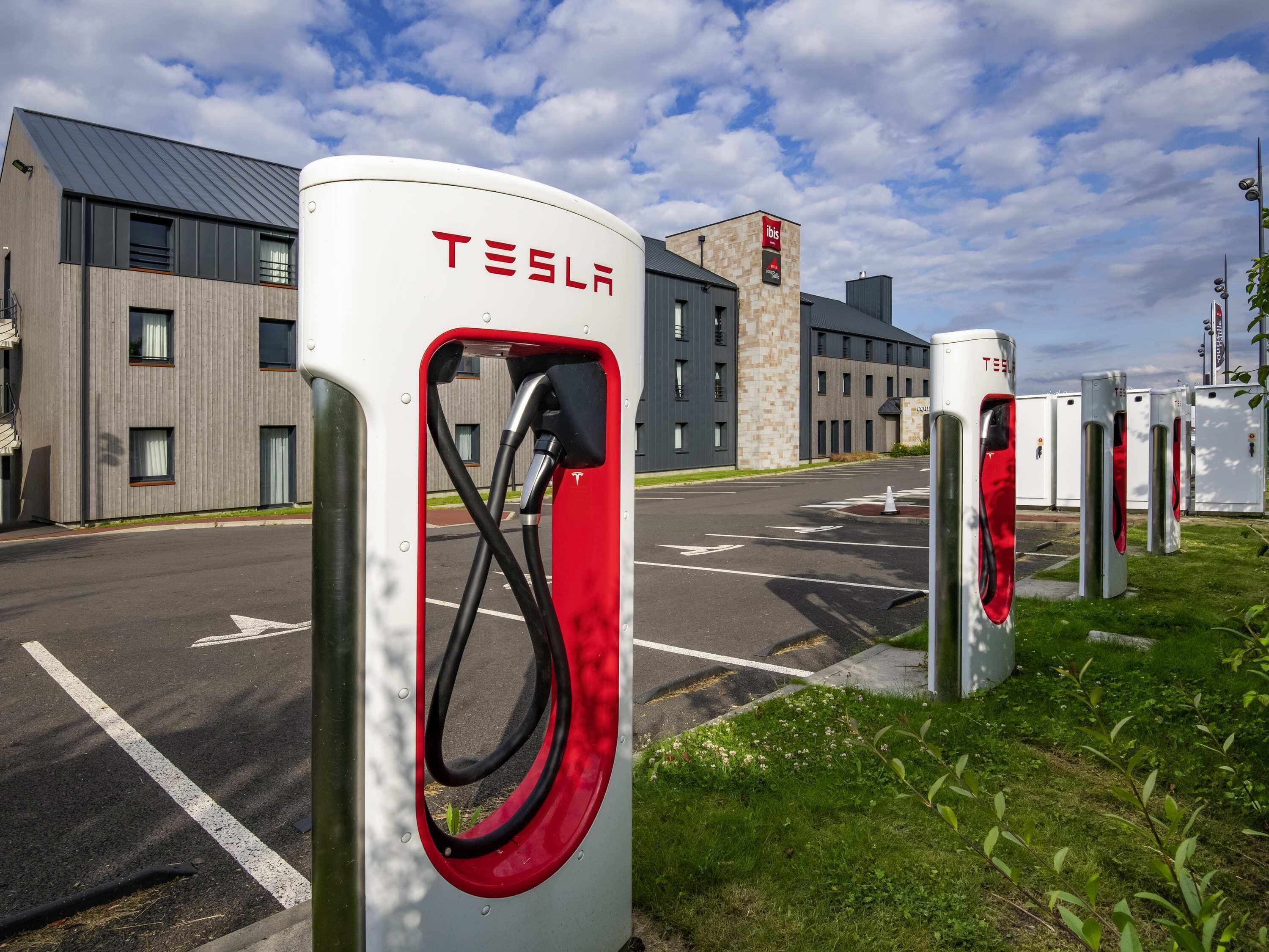 Une borne de recharge Tesla avec un bâtiment moderne en arrière-plan.