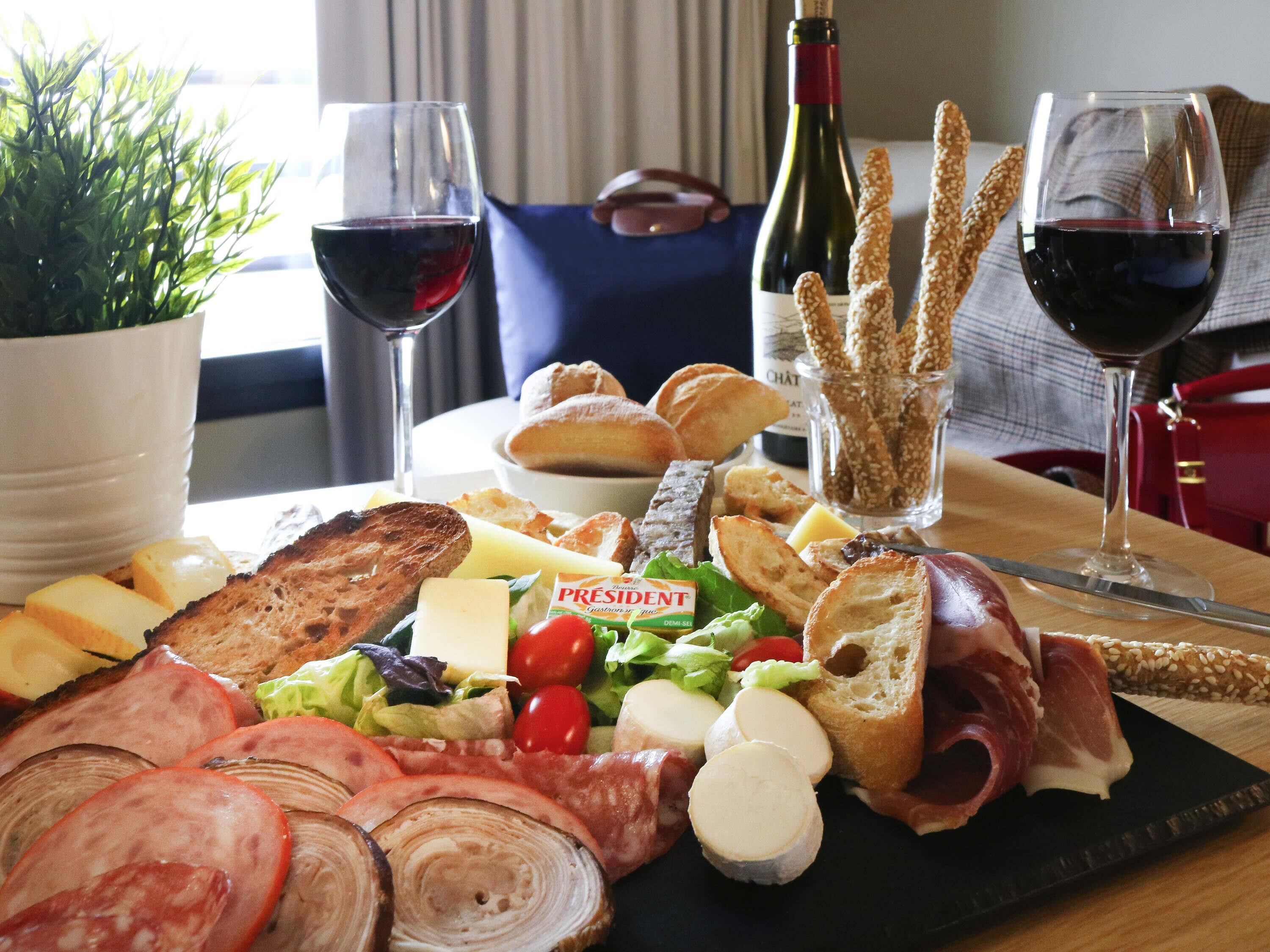 Une planche de charcuterie avec divers types de viandes, de fromages et de pain, accompagnée de verres à vin et d’une bouteille de vin.