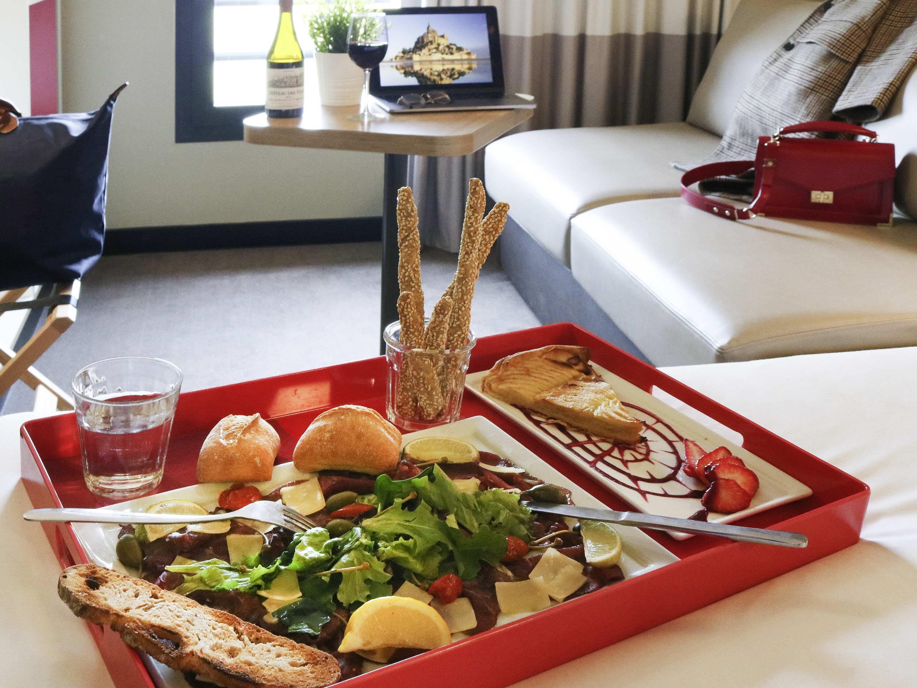 Een dienblad met salade, brood en een dessert, staand op een rood dienblad in een hotelkamer.