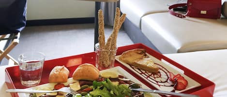 Een dienblad met salade, brood en een dessert, staand op een rood dienblad in een hotelkamer.