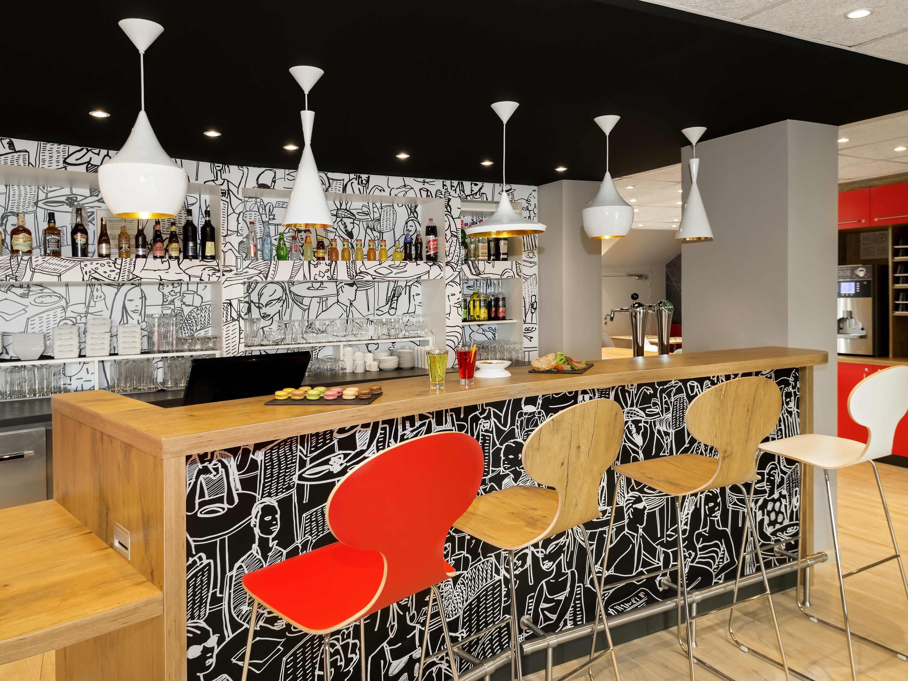 A modern bar area with a black and white mural, white pendant lights, and a variety of bottles and glasses on shelves.