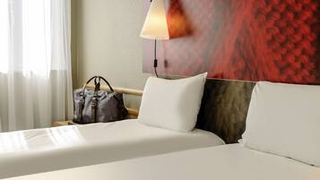 Une chambre d’hôtel avec un lit bien fait, une lampe suspendue et un mur orné d’un motif texturé.