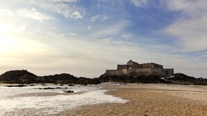 A historic stone building on a rocky beach with a clear sky.