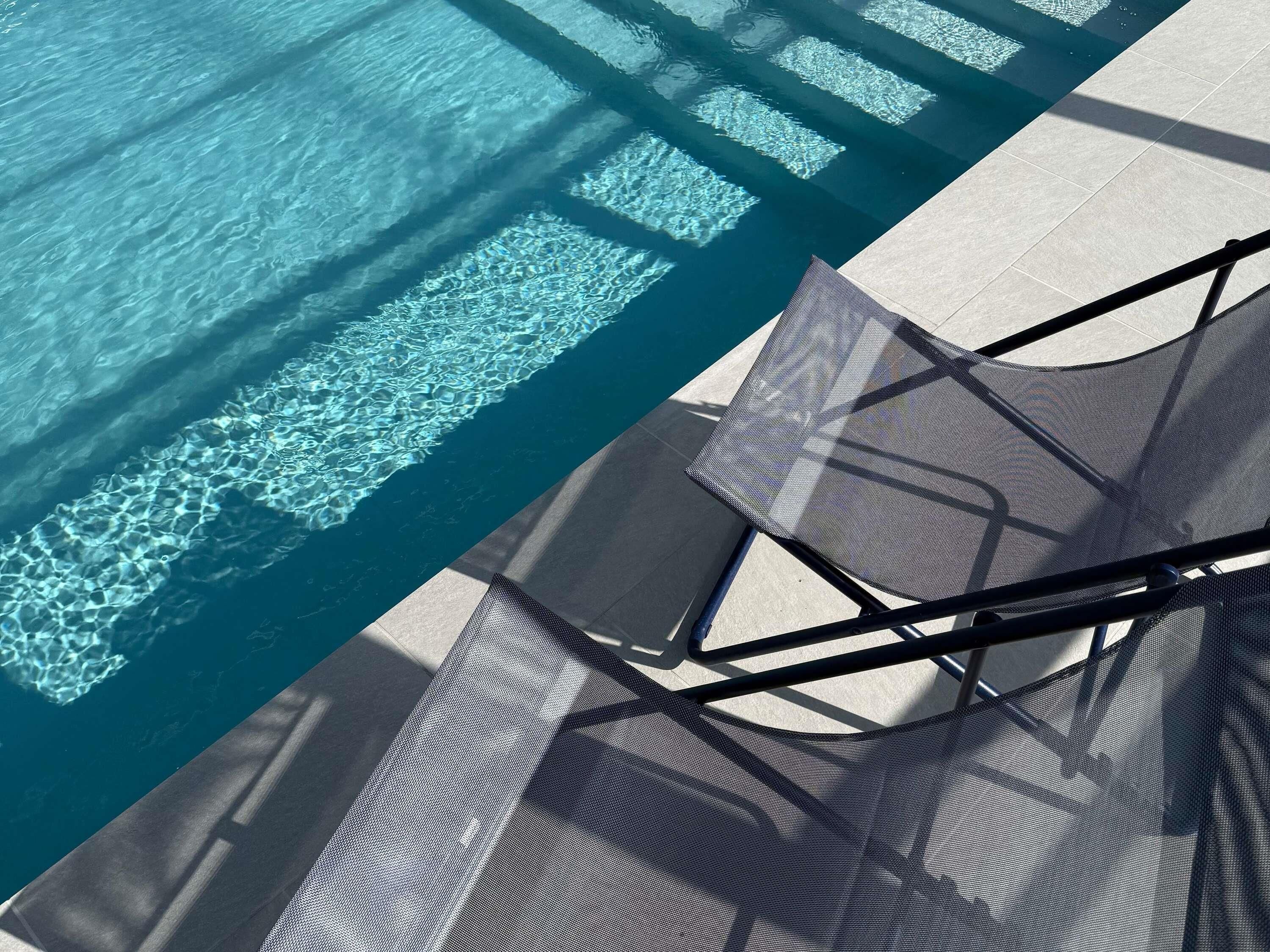 A poolside area with clear water, a tiled deck, and a chair with a mesh backrest.