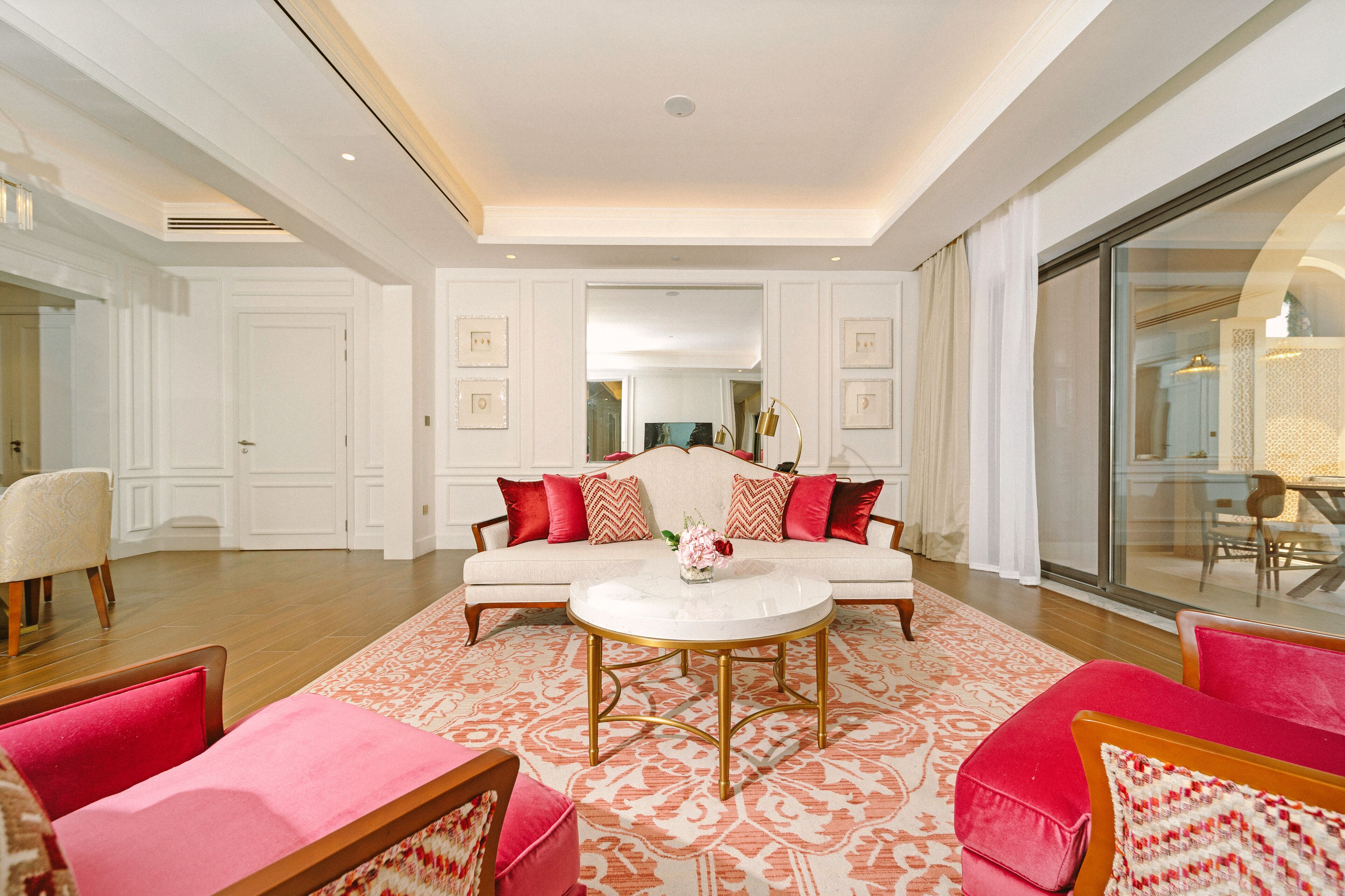 A spacious living room with a white sofa, red cushions, and a round coffee table.