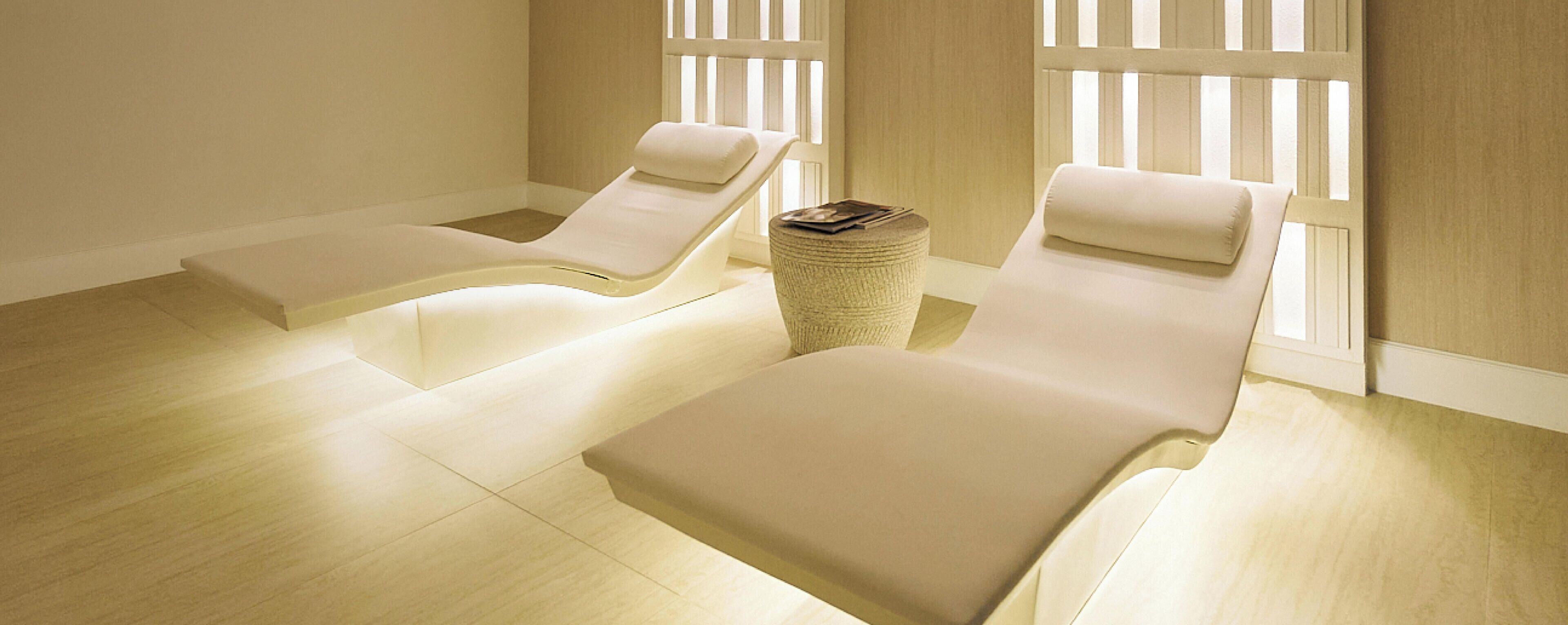 A room with two reclining chairs, a small round table, and a window with vertical blinds.