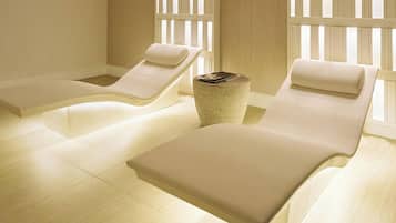 A room with two reclining chairs, a small round table, and a window with vertical blinds.