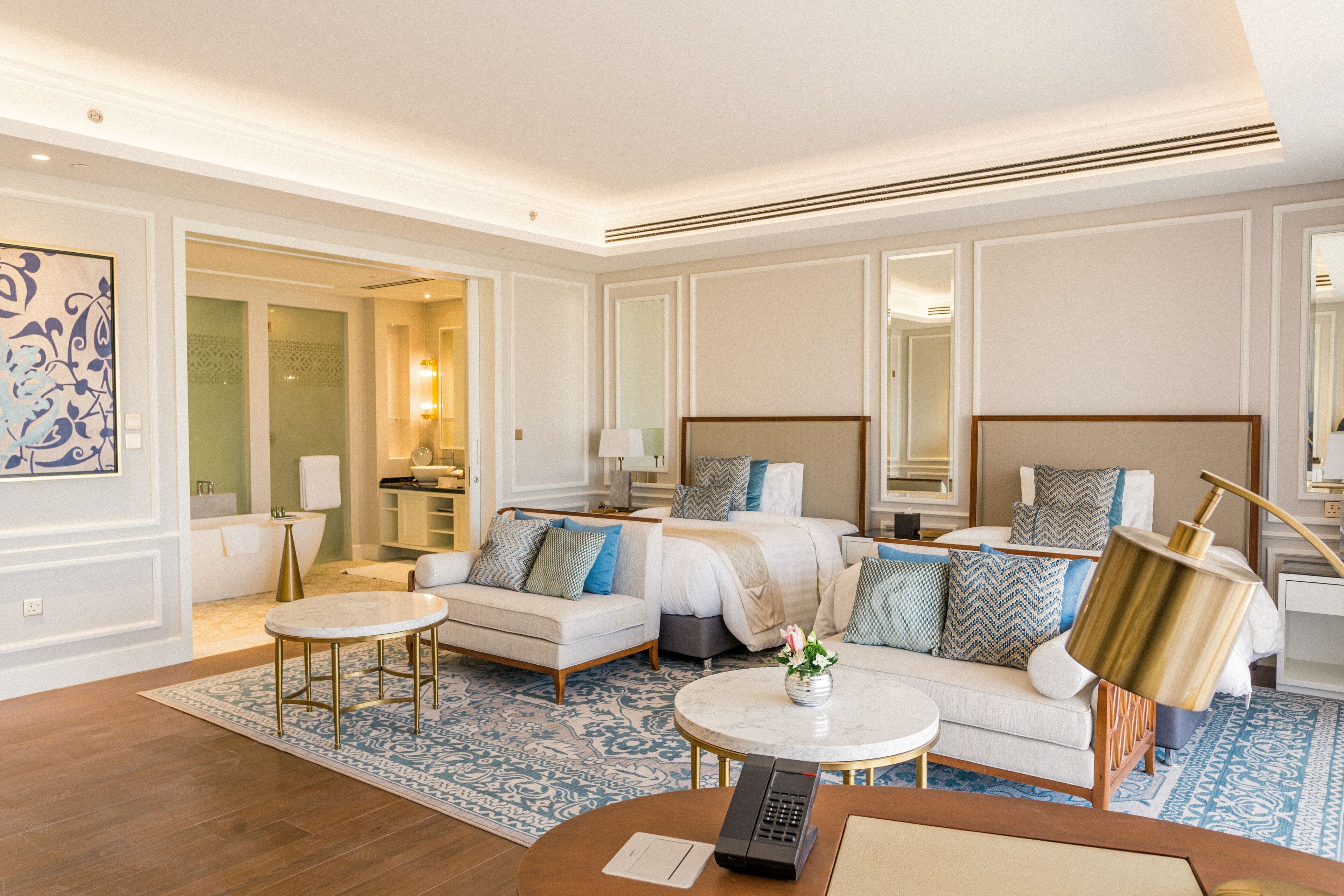 Habitación de hotel con una cama grande, dos sofás, una mesita de café y un baño visible a través de una puerta abierta.